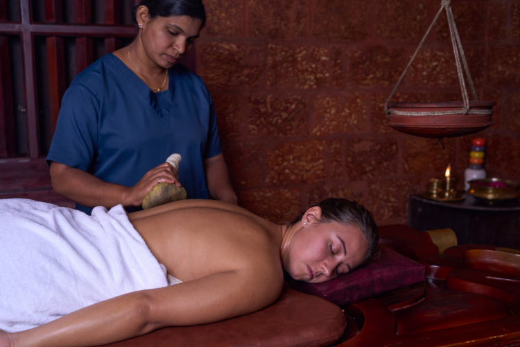 "Guest receiving Kizhi therapy at Indeevara AyurYoga Retreat, where warm herbal poultices are gently massaged over the body to relieve muscle tension and improve circulation.